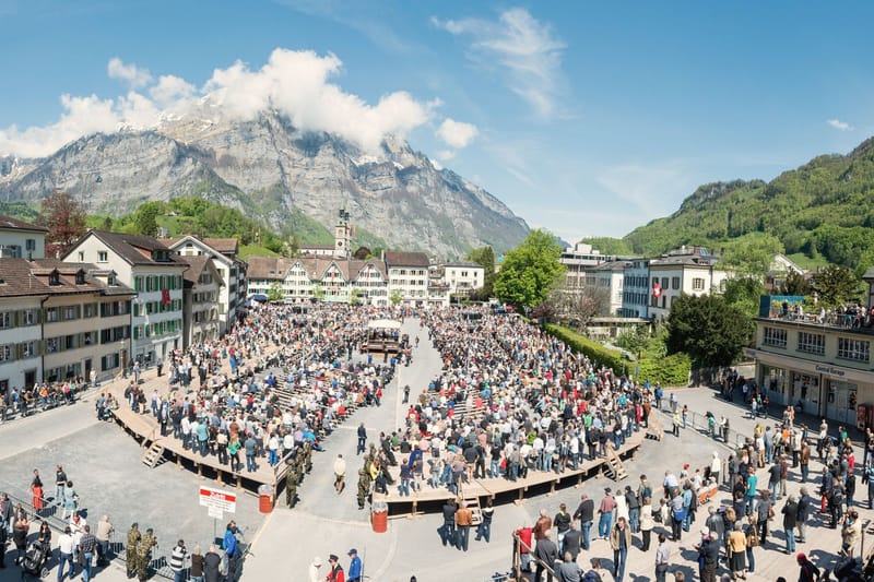 Thousands of residents gather in a town square ringed by houses and mountains for an open-air assembly in Glarus, Switzerland.